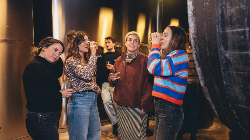 A group of young people tasting cider among the tanks and casks of the Begiristain cellar