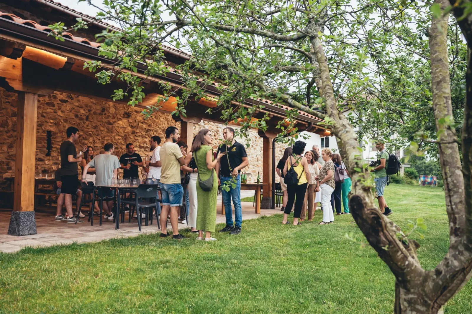 A group chatting with glasses of cider on Mizpiradi’s stone and timber porch, next to an apple tree