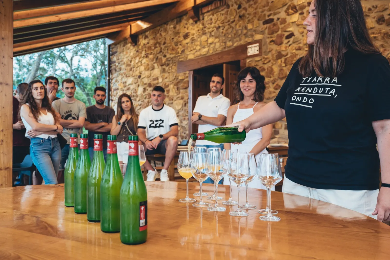 A guide pours cider into glasses in front of a group, with Mizpiradi bottles on a wooden table