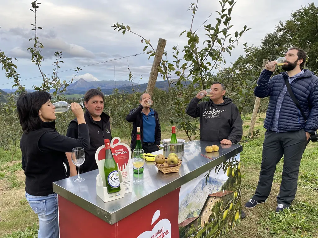 Oiharte cider tasting at a bar set up in the orchard, with mountains in the background