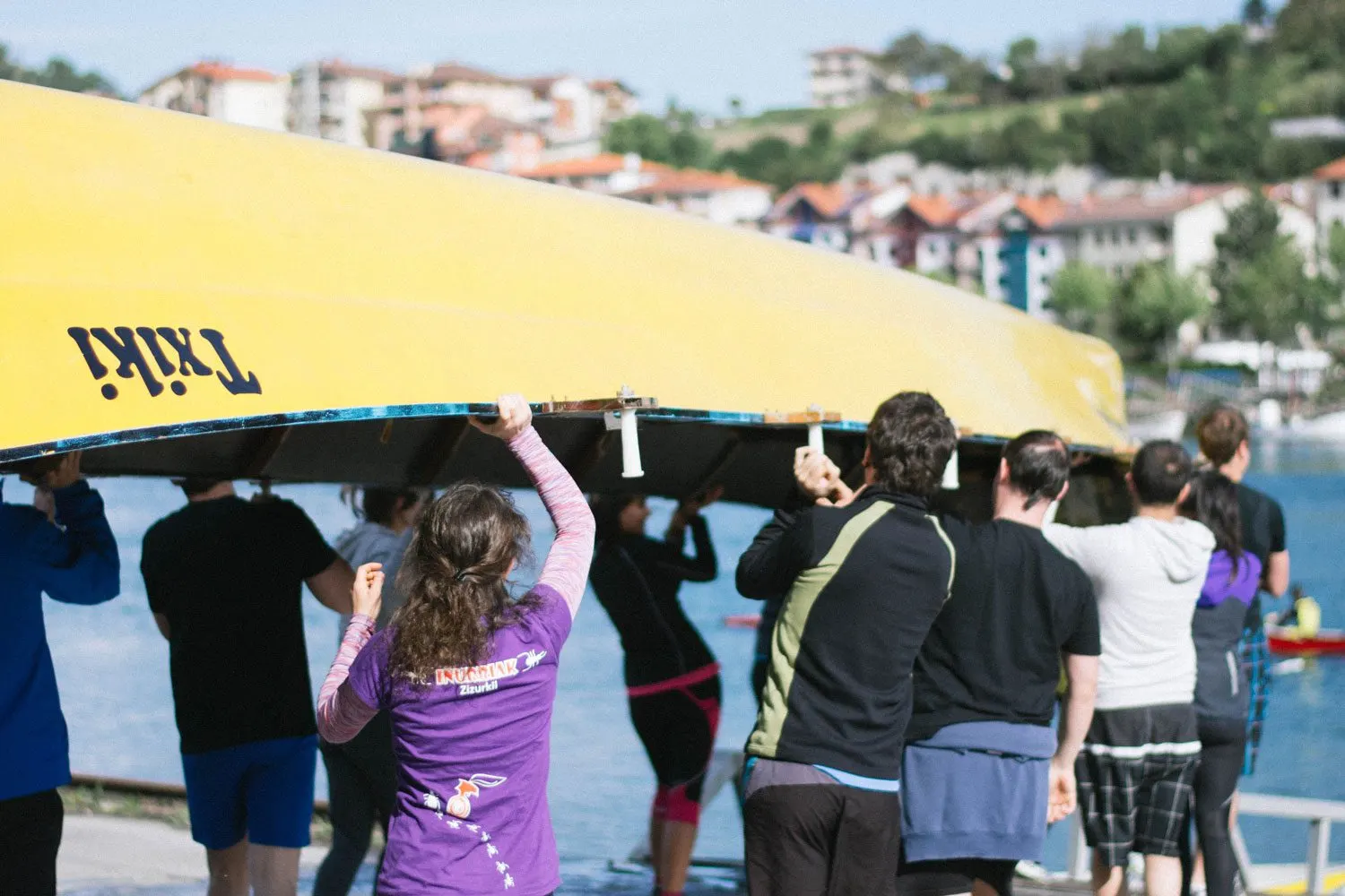 Group of participants carrying a yellow rowing boat beside the Orio estuary