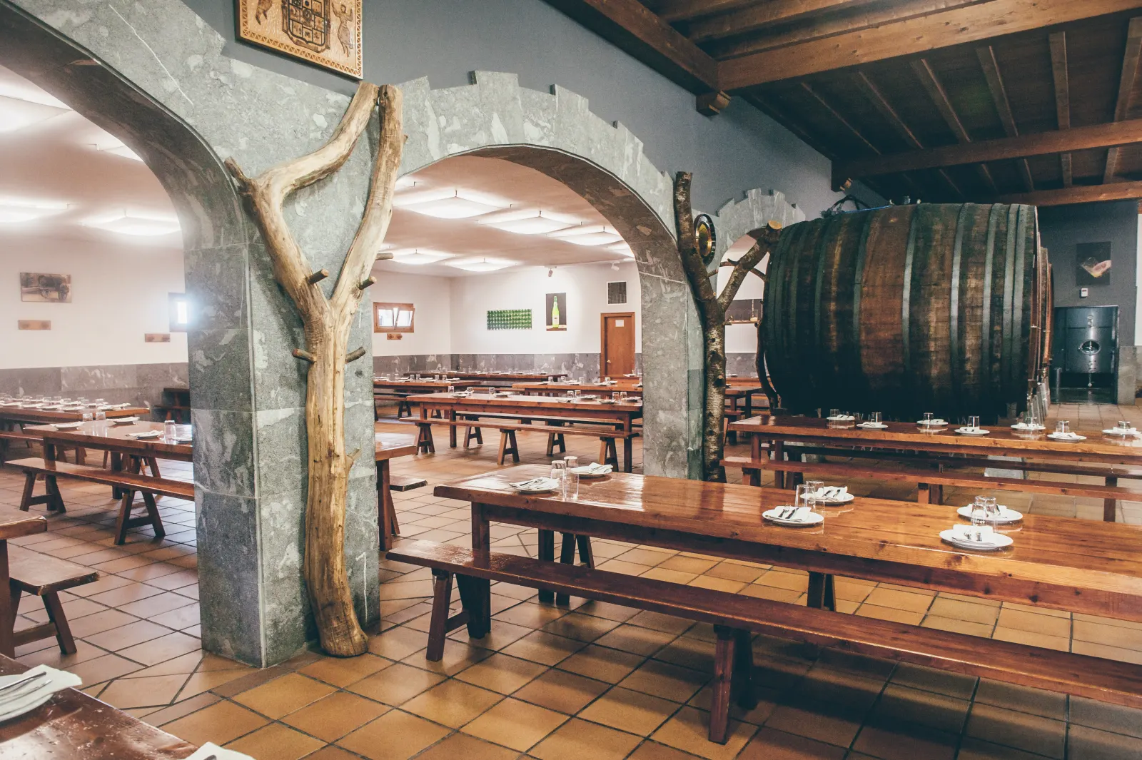 Comedor de la sidrería Aburuza, con mesas corridas de madera, arcos de piedra y una kupela al fondo