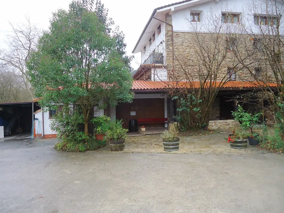 Edificio de piedra de la sidrería Aialde Berri en Usurbil, con un patio con árboles y barricas usadas como maceteros
