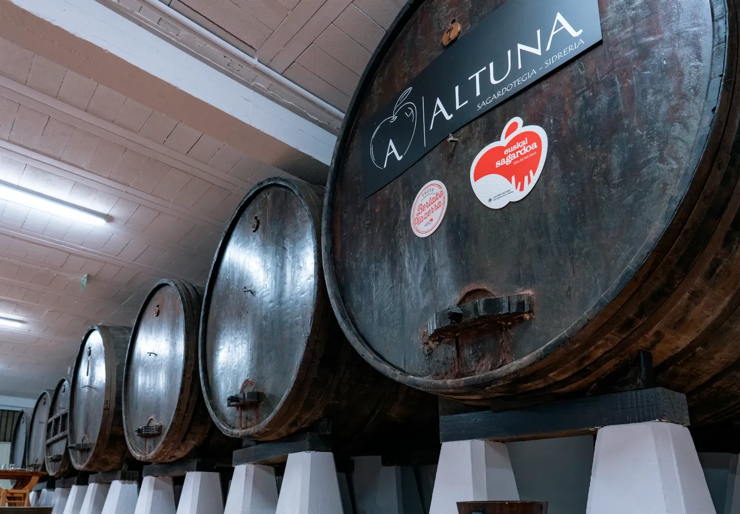 Fila de kupelas en la bodega de la sidrería Altuna, la primera con el logotipo de la casa