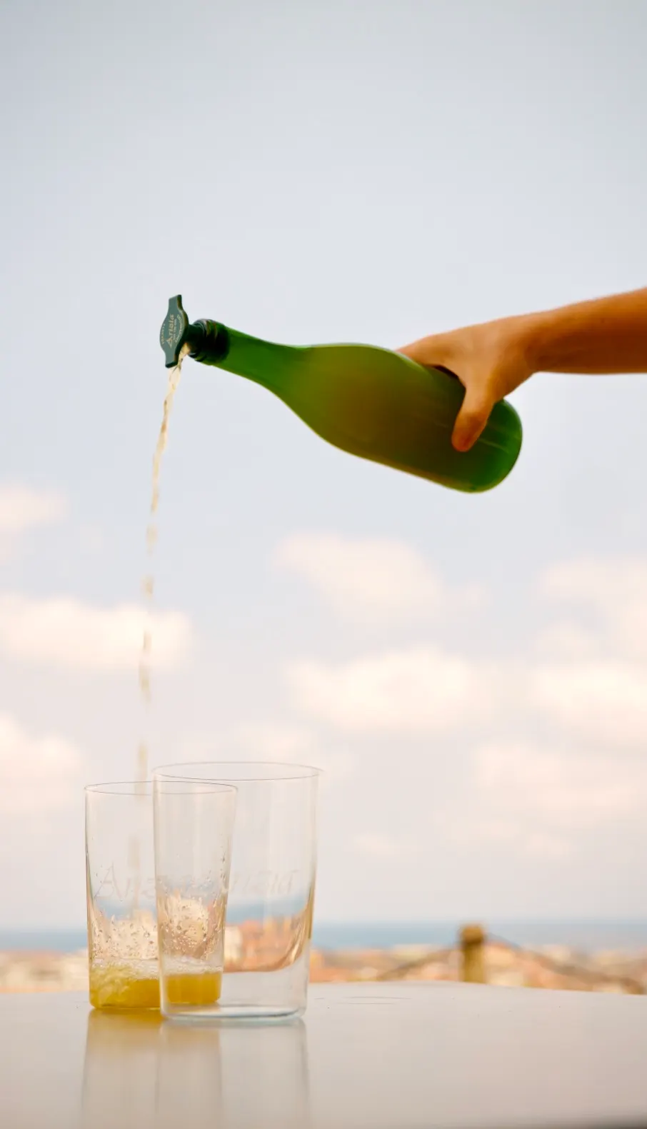 Sidra Arizia escanciada desde la botella a dos vasos, con Zarautz y el mar al fondo