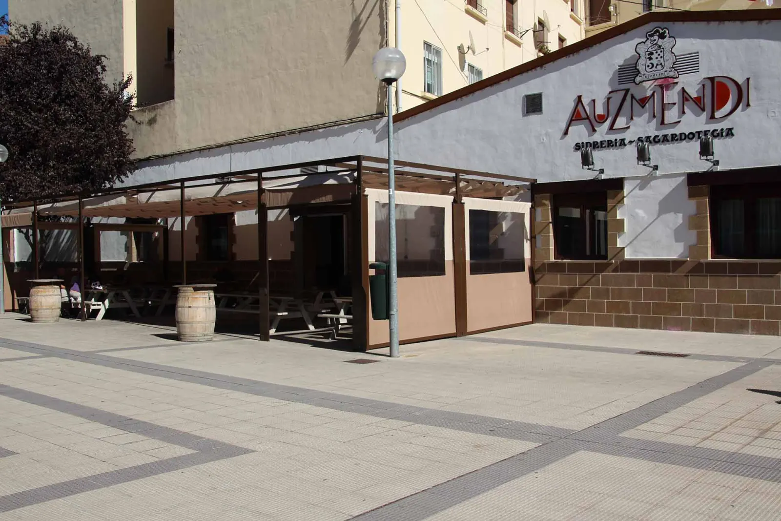 Fachada de la sidrería Auzmendi en Pamplona, con su terraza cubierta y barricas en la acera
