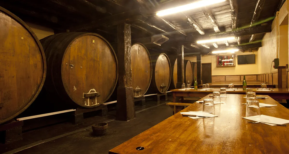 Comedor de la sidrería Begiristain, con una mesa larga de madera preparada junto a una fila de kupelas