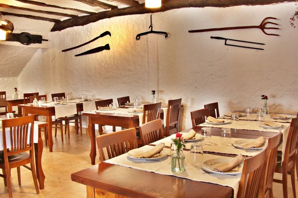 Comedor de la sidrería Egiluze, con mesas de madera puestas, paredes encaladas, vigas y aperos antiguos colgados