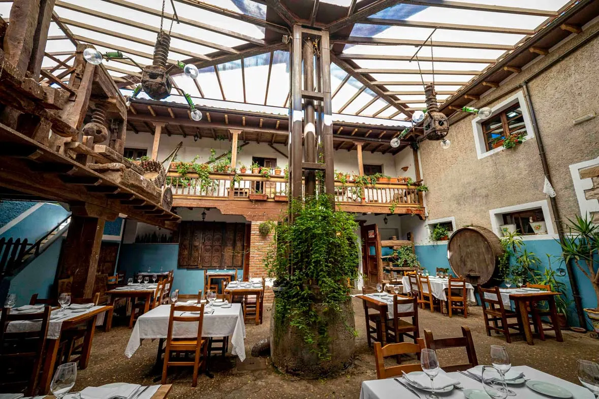 Patio interior cubierto con mesas, vigas de madera y un tonel