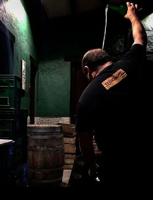 A man pours cider from height next to a barrel in the cider mill