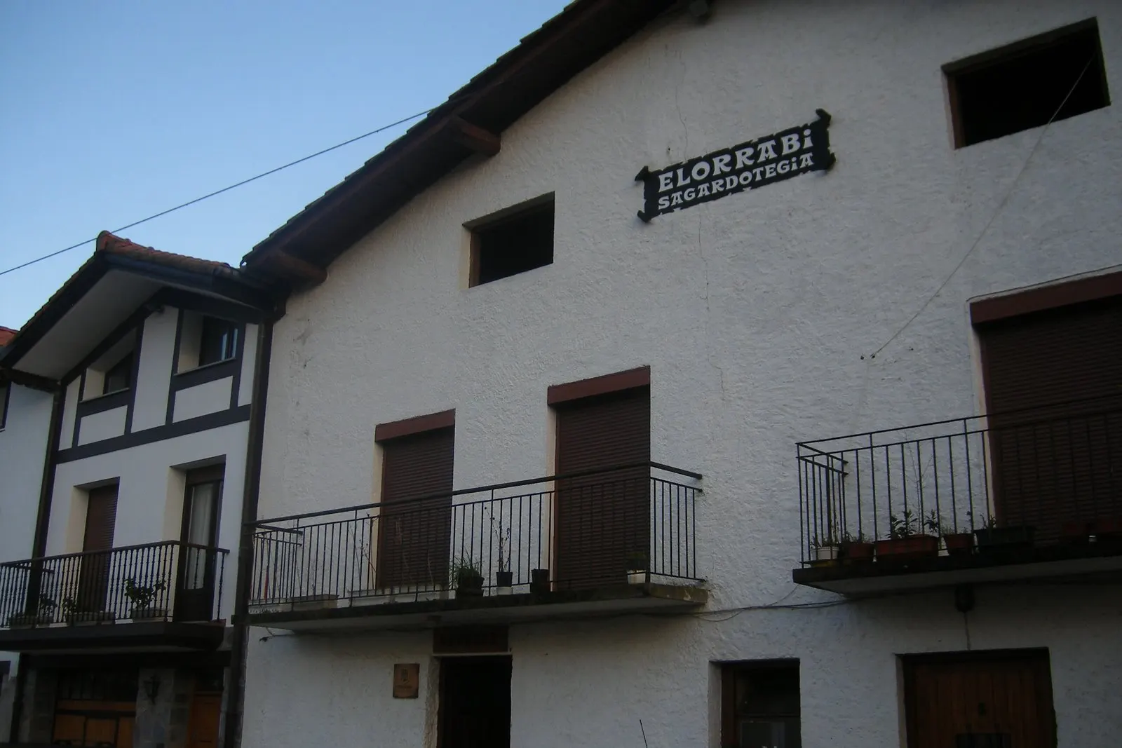 Fachada blanca del caserío de la sidrería Elorrabi, con balcones y el letrero «Elorrabi Sagardotegia»