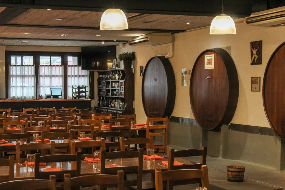 Dining room of the Intxaurrondo cider house, with laid wooden tables and kupelas set into the wall
