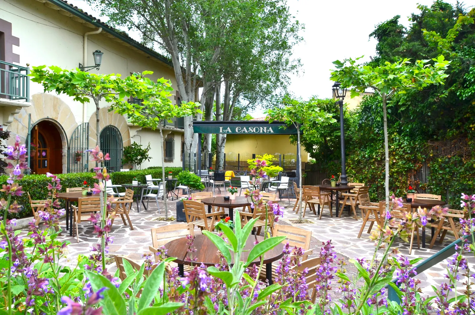 Garden terrace of the La Casona cider house in Barañain, with wooden tables among trees and flowers