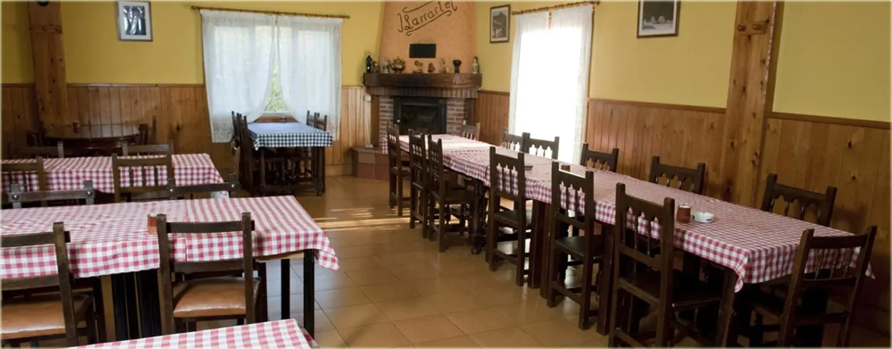 Comedor de la sidrería Larrarte, con mesas de mantel de cuadros rojos, sillas de madera y una chimenea al fondo