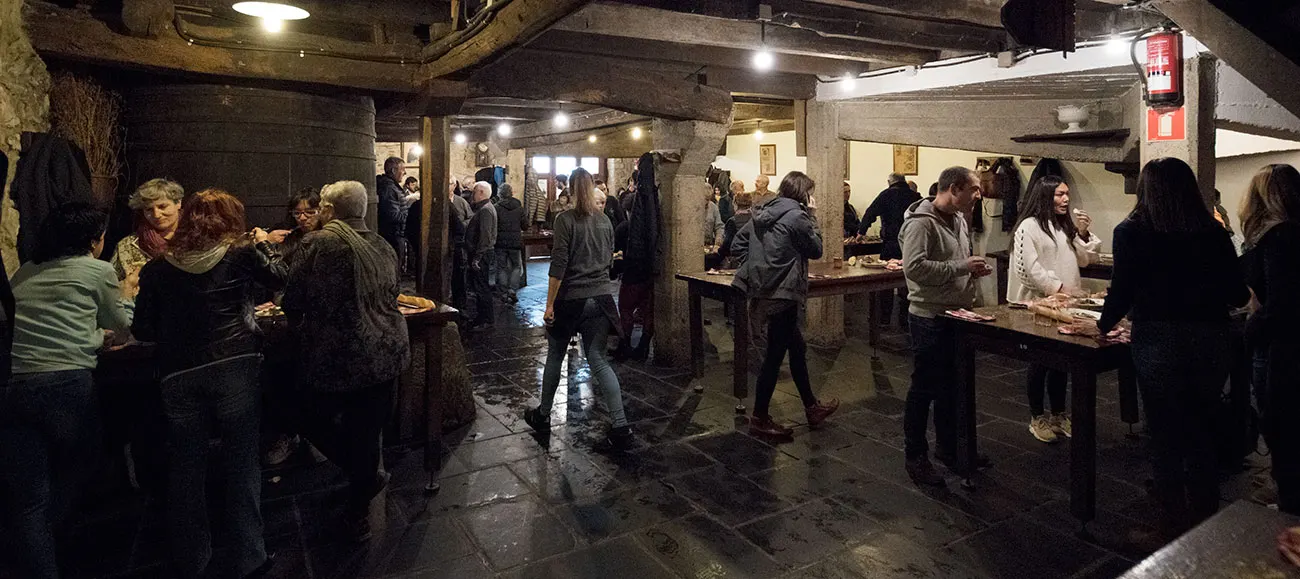 Comedor de la sidrería Lizeaga lleno de gente comiendo de pie junto a las mesas