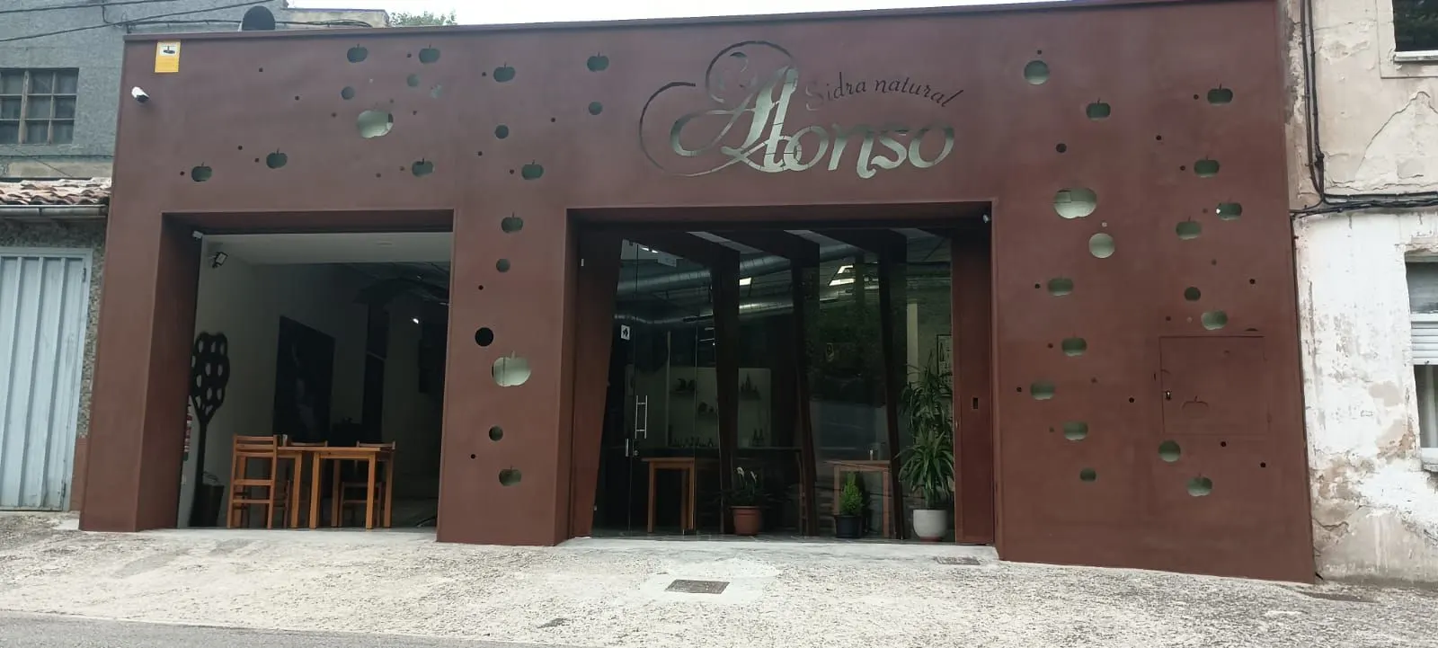 Fachada del llagar con el rótulo «Sidra natural Alonso» y siluetas de manzanas caladas en la chapa