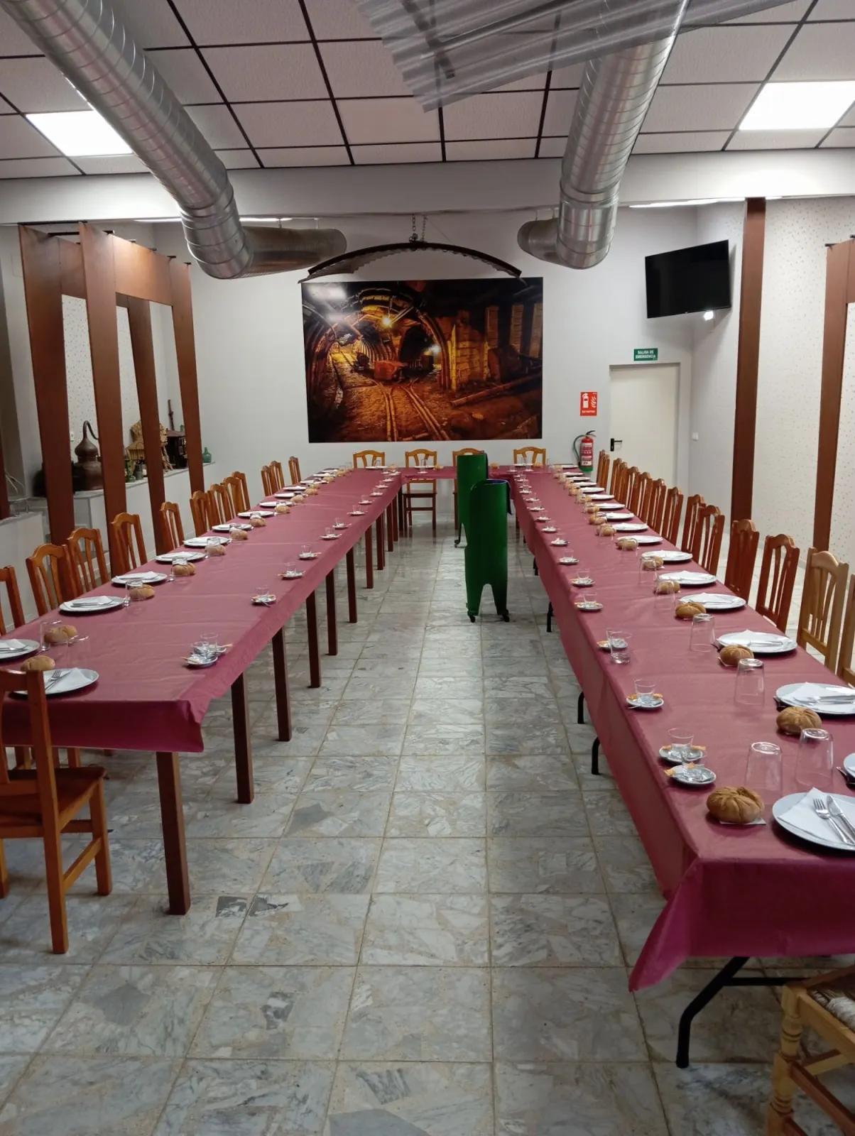 Comedor con mesas largas montadas para una espicha y una gran fotografía de una galería minera al fondo