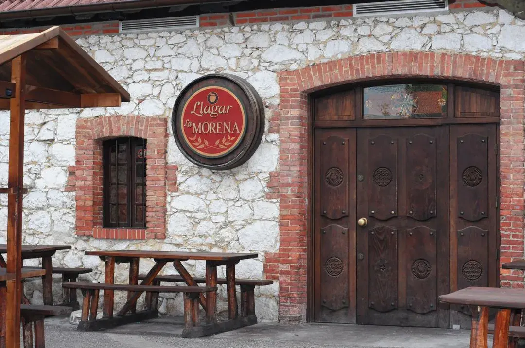 Fachada de piedra y ladrillo del Llagar La Morena con mesas de madera