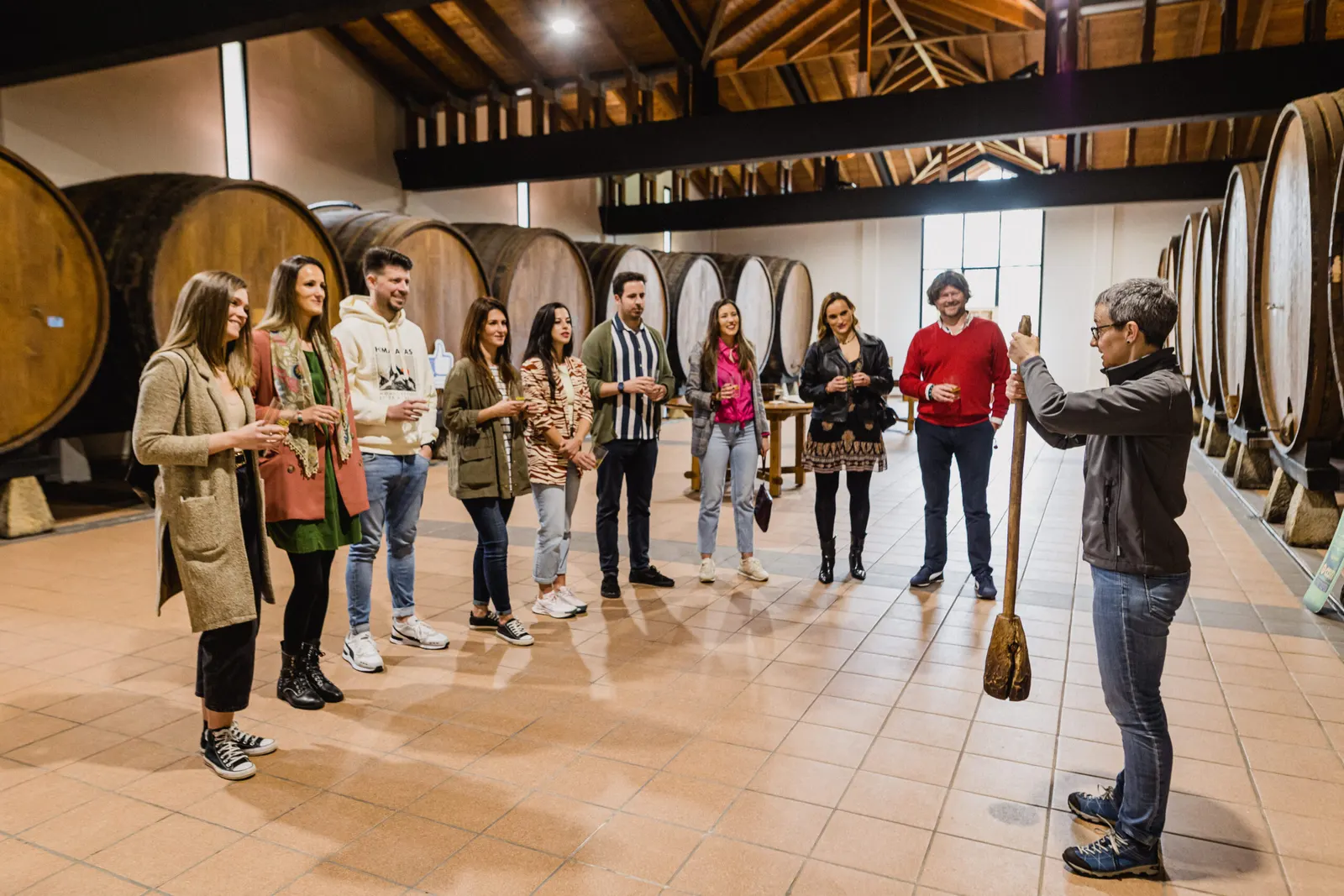 Grupo de visitantes en la bodega de toneles del Llagar Castañón mientras la guía escancia