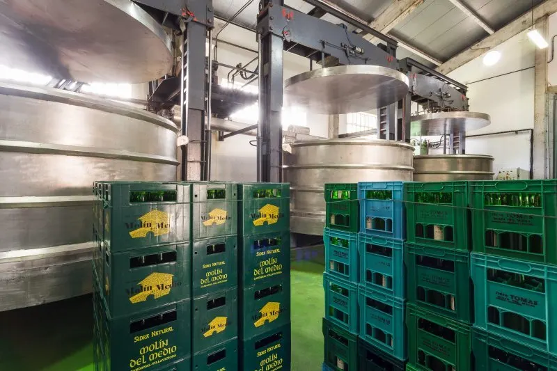 Stainless steel presses and stacked crates of Molín del Medio and J. Tomás bottles