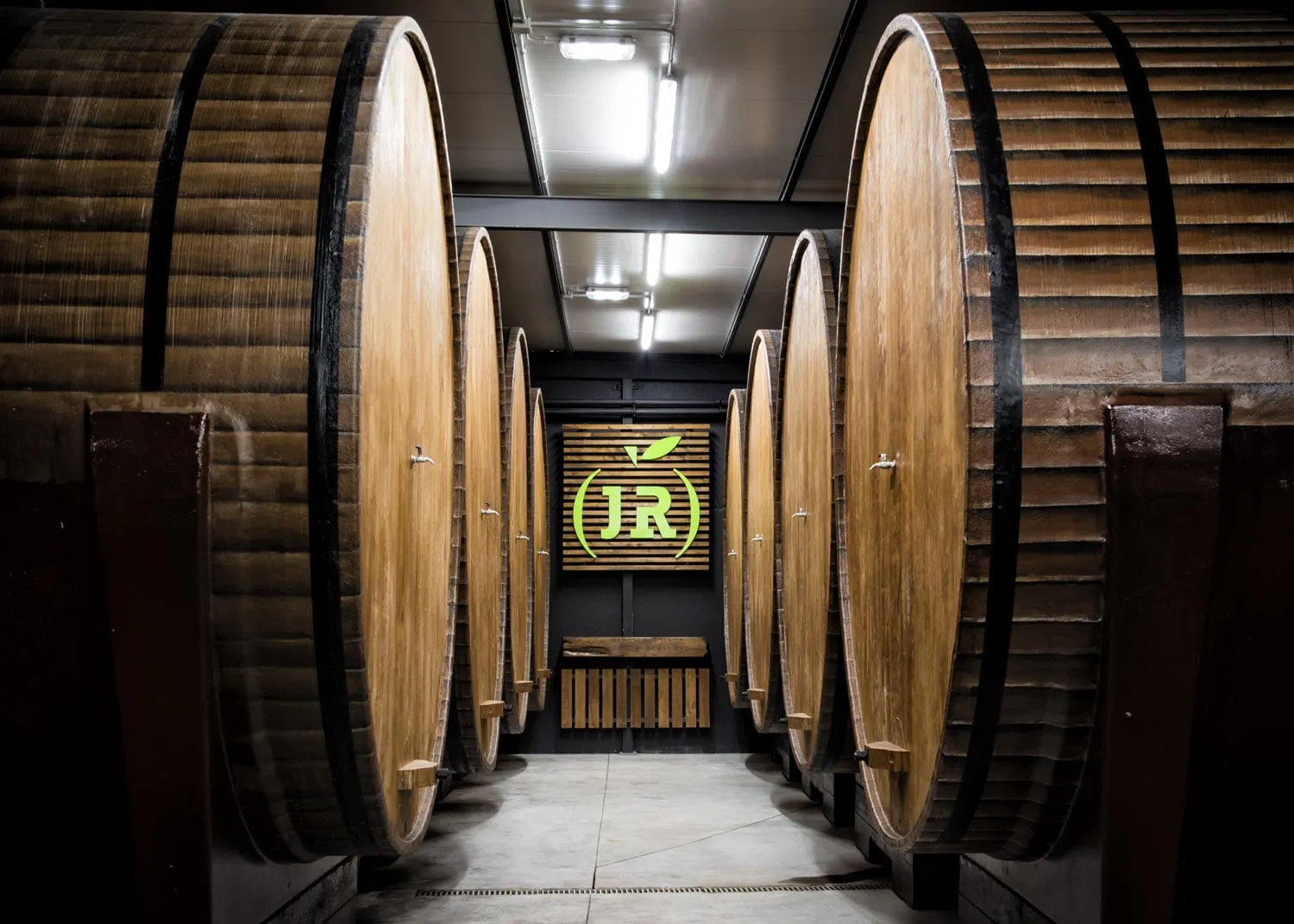 Pasillo de grandes toneles de madera en el llagar de Sidra JR, con el logotipo al fondo