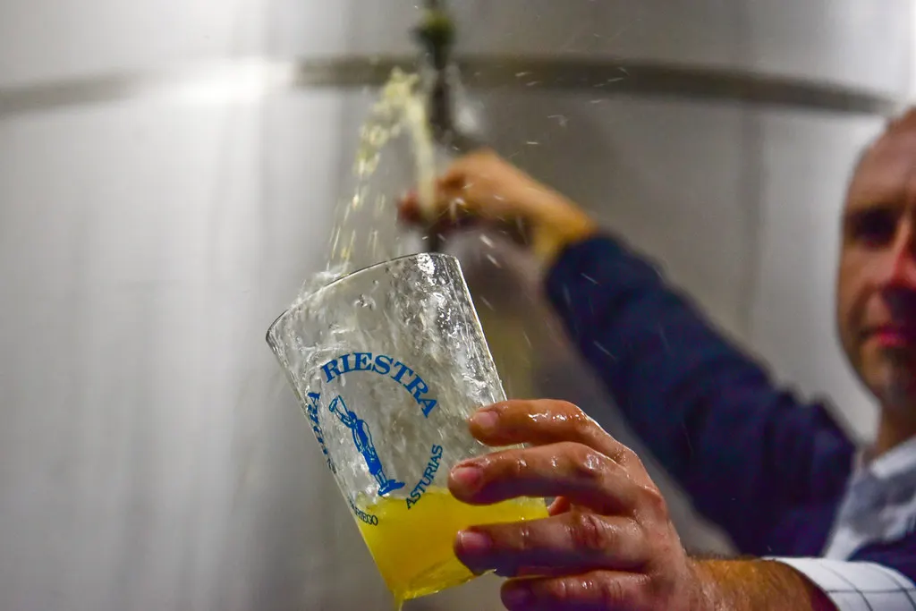 Un verre au logo de Riestra se remplit de cidre depuis une cuve