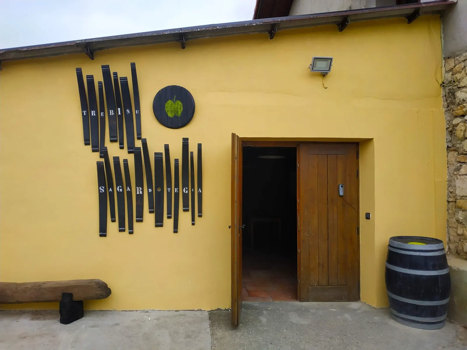 Entrada de la sidrería Trebiñu, con la fachada amarilla y una barrica junto a la puerta