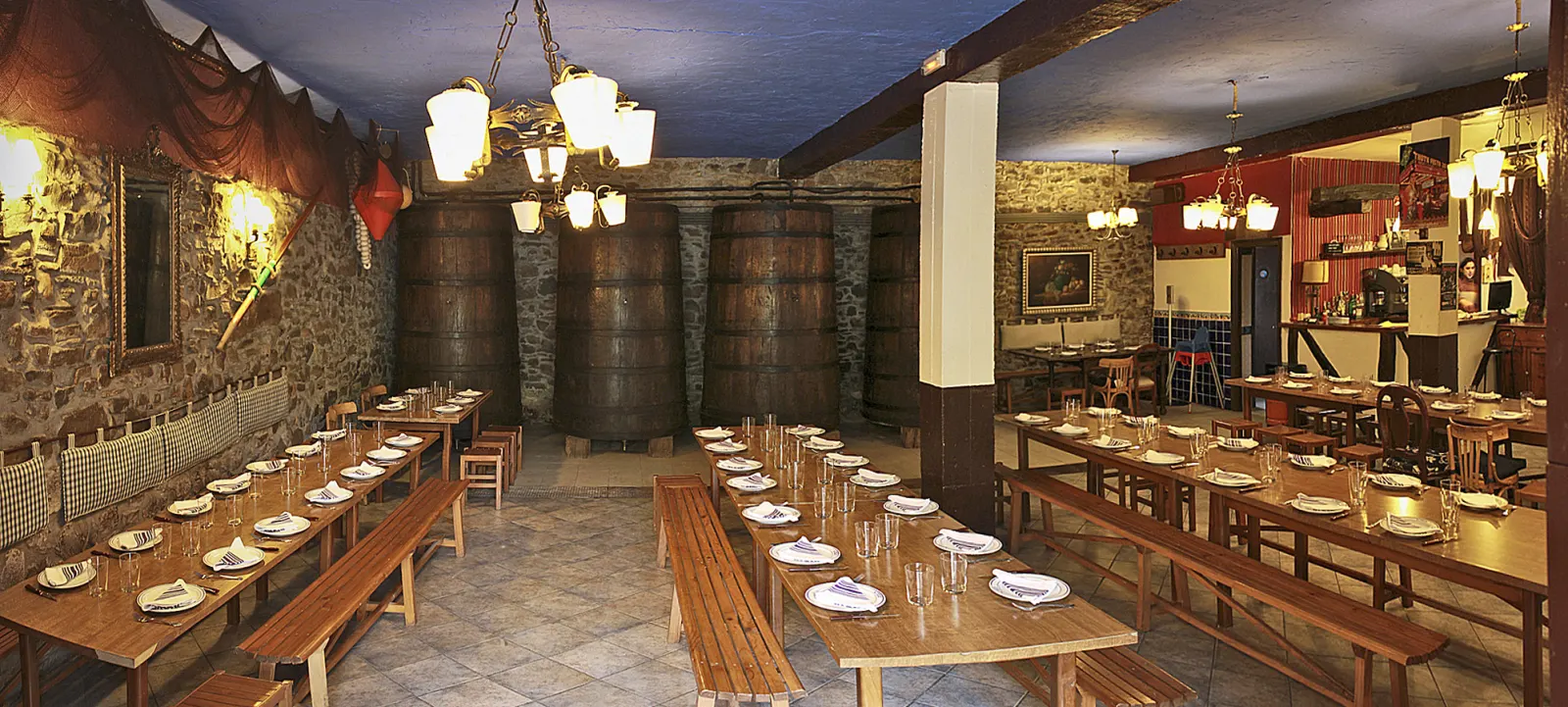 Comedor de la sidrería Txindurri Iturri, con paredes de piedra, mesas corridas puestas y kupelas al fondo