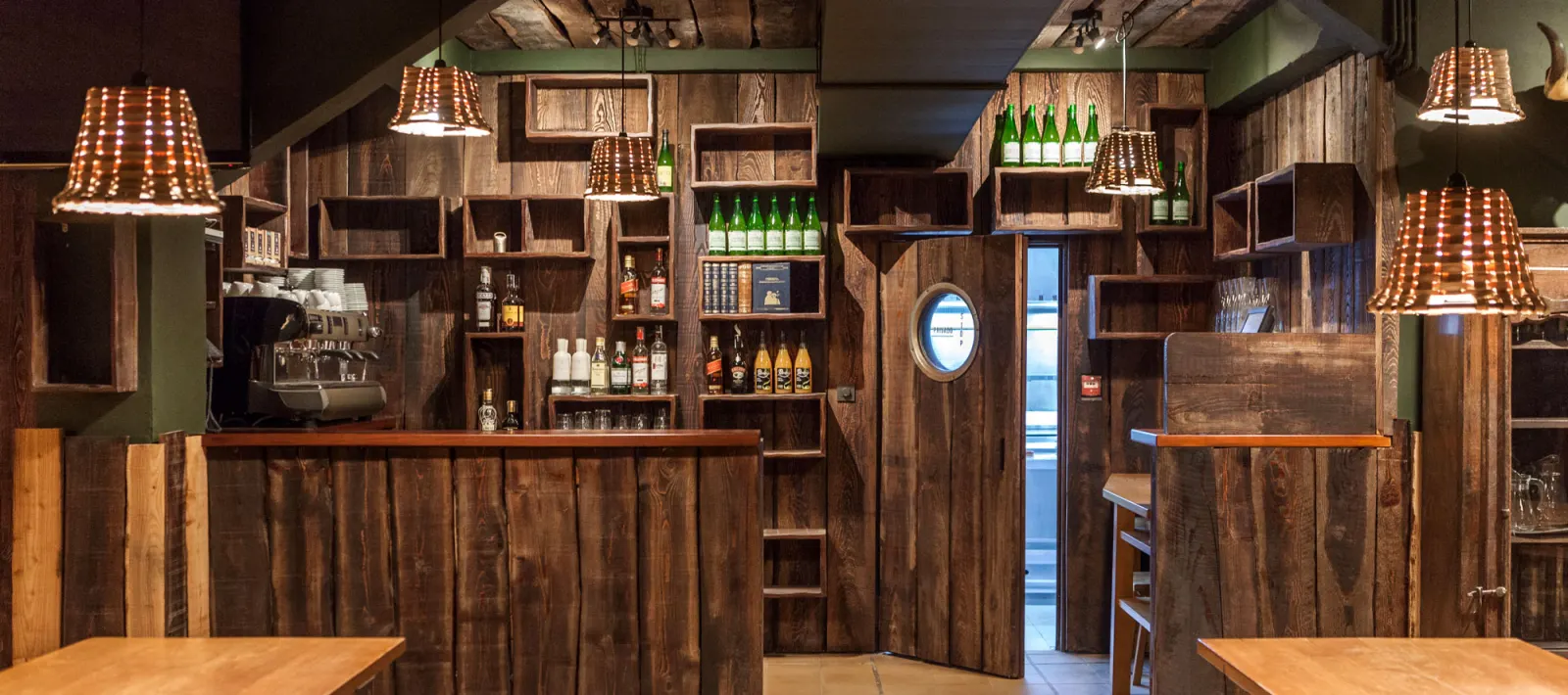 Inside Txirrita Sagardotegia, with a rustic wooden bar and shelves full of cider bottles under wicker lamps