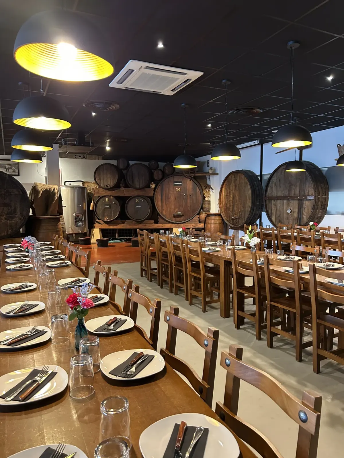 Comedor de la Cidrerie Berri en Ascain, con largas mesas puestas y kupelas de madera en el chai del fondo